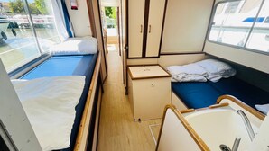 Un intérieur compact et bien éclairé, comprenant deux lits, une petite kitchenette et une fenêtre donnant sur l’extérieur.