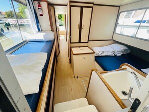 A compact, well-lit interior with two beds, a small kitchenette, and a window providing a view of the outside. - Spacious boat with water view - 8 guests (Colombiers)