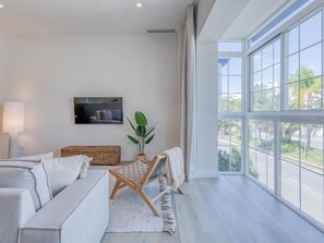 Ein modernes Wohnzimmer mit einer Couch, einem Fernseher, einer Pflanze und Blick ins Freie.