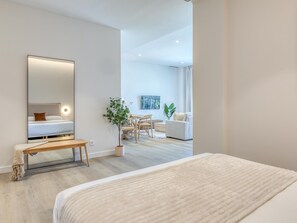 Ein modernes Hotelzimmer mit einem großen Bett, einer Bank, einem kleinen Tisch, einer Topfpflanze und Blick auf den Wohnbereich.
