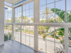 Ein Zimmer mit großen Fenstern, Holzboden und Blick auf eine Straße mit Palmen und Gebäuden.