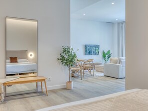 Ein modernes Hotelzimmer mit Bett, Nachttisch, Spiegel, Topfpflanze, Essbereich und einer Couch.