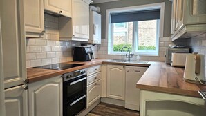 A kitchen with white cabinets, a built-in oven, a stovetop, a sink, and a window with a view of greenery outside. - Beach Horizon - ground floor flat with patio boasting views to sea (Pevensey Bay)