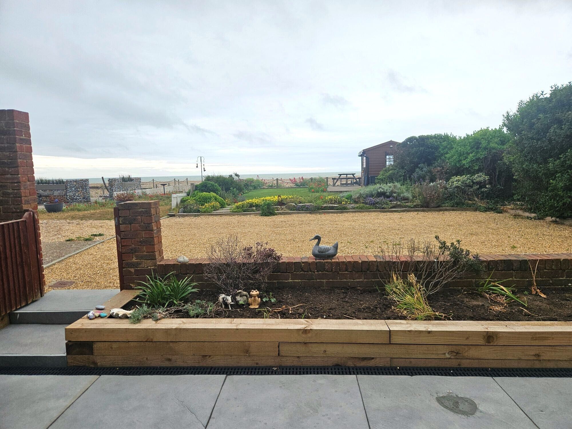 A garden with a swan statue, a wooden bench, and a brick wall.