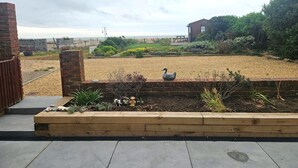 A garden with a swan statue, a wooden bench, and a brick wall. - Beach Horizon - ground floor flat with patio boasting views to sea (Pevensey Bay)