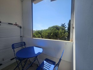 Ein Balkon mit Tisch und Stühlen, ein Fenster mit Blick auf Bäume und eine weiße Wand.