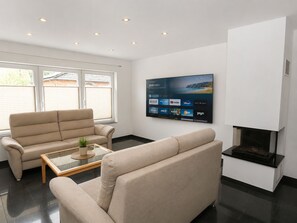 Ein modernes Wohnzimmer mit einem beigefarbenen Sofa, einem Glastisch, einem flachbildfernseher an der Wand und einem Kamin.