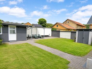 Ein wohnlicher Garten mit gepflasterter Terrasse, überdachter Sitzgelegenheit und umzäunter Grundstück.
