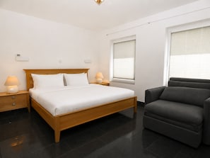 Ein modernes Hotelzimmer mit einem hölzernen Bett, zwei Nachttischlampen, einem dunklen Sofa und einem Fenster mit Jalousien.