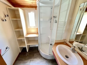 A bathroom with a glass shower enclosure, a sink, and built-in shelving.