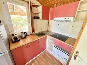 Pieni, käytännöllinen keittiönurkkaus, jossa on pesuallas, liesi ja vedenkeitin työtasolla.