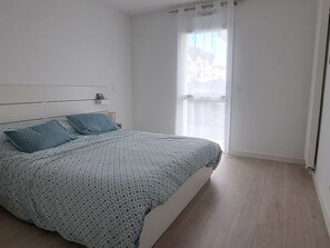 Ein Schlafzimmer mit Bett, einem Fenster mit Vorhängen und Blick auf Gebäude.