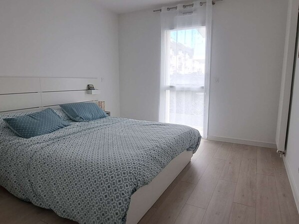 A bedroom with a bed, a window with curtains, and a view of buildings outside. - Comfortable apartment with parking - 4/5 guests (Carnac)