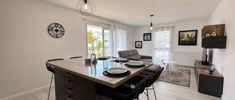 A modern kitchen with a central island, dining area with chairs, and a living space with a sofa and a coffee table.