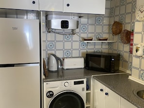 Eine kleine Küche mit Waschmaschine, Mikrowelle, Toaster und Wasserkocher.