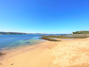 Ein Strand mit klarem Wasser, einem Sandufer und einer entfernten Hügelkuppe mit einer Bebauung.