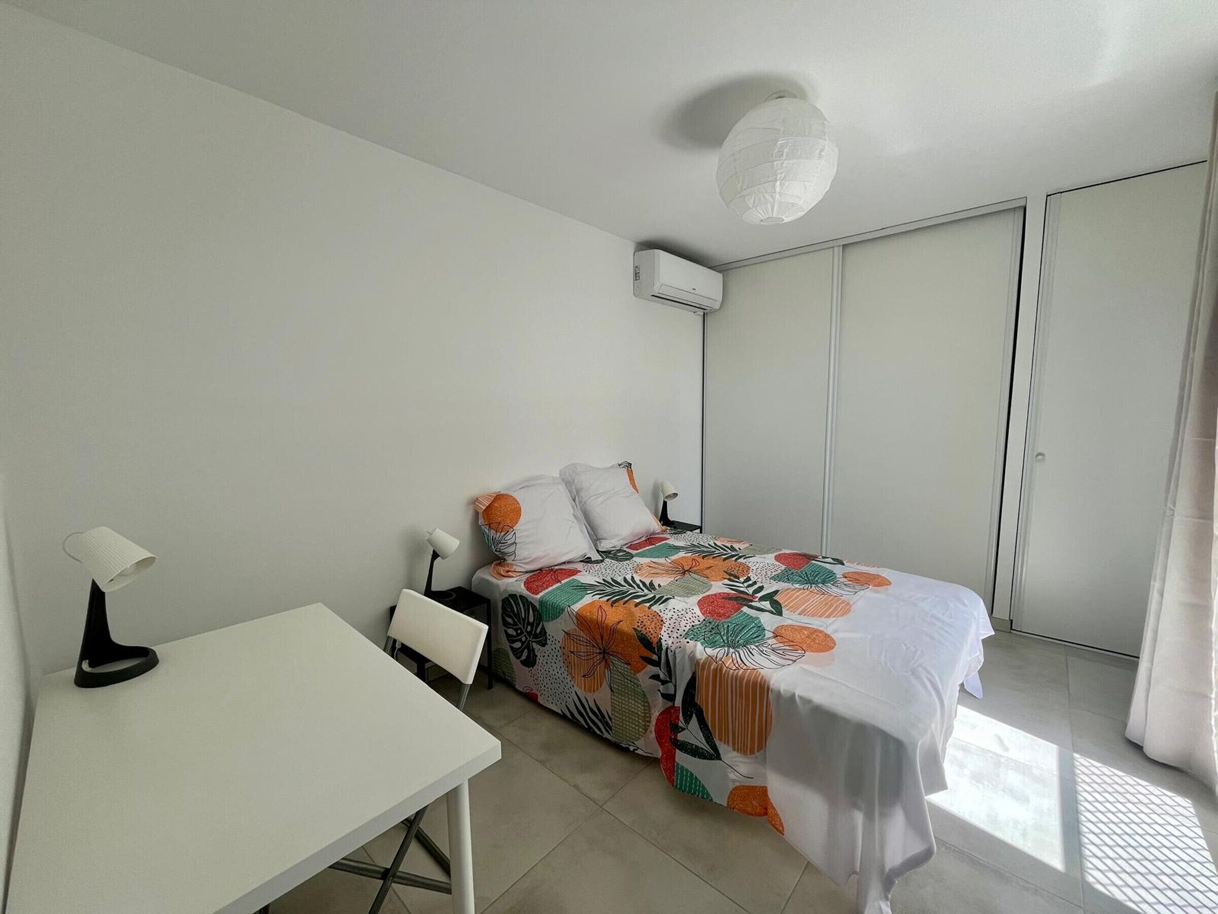 A bedroom with a bed, a desk, a chair, a ceiling light, and a wardrobe.