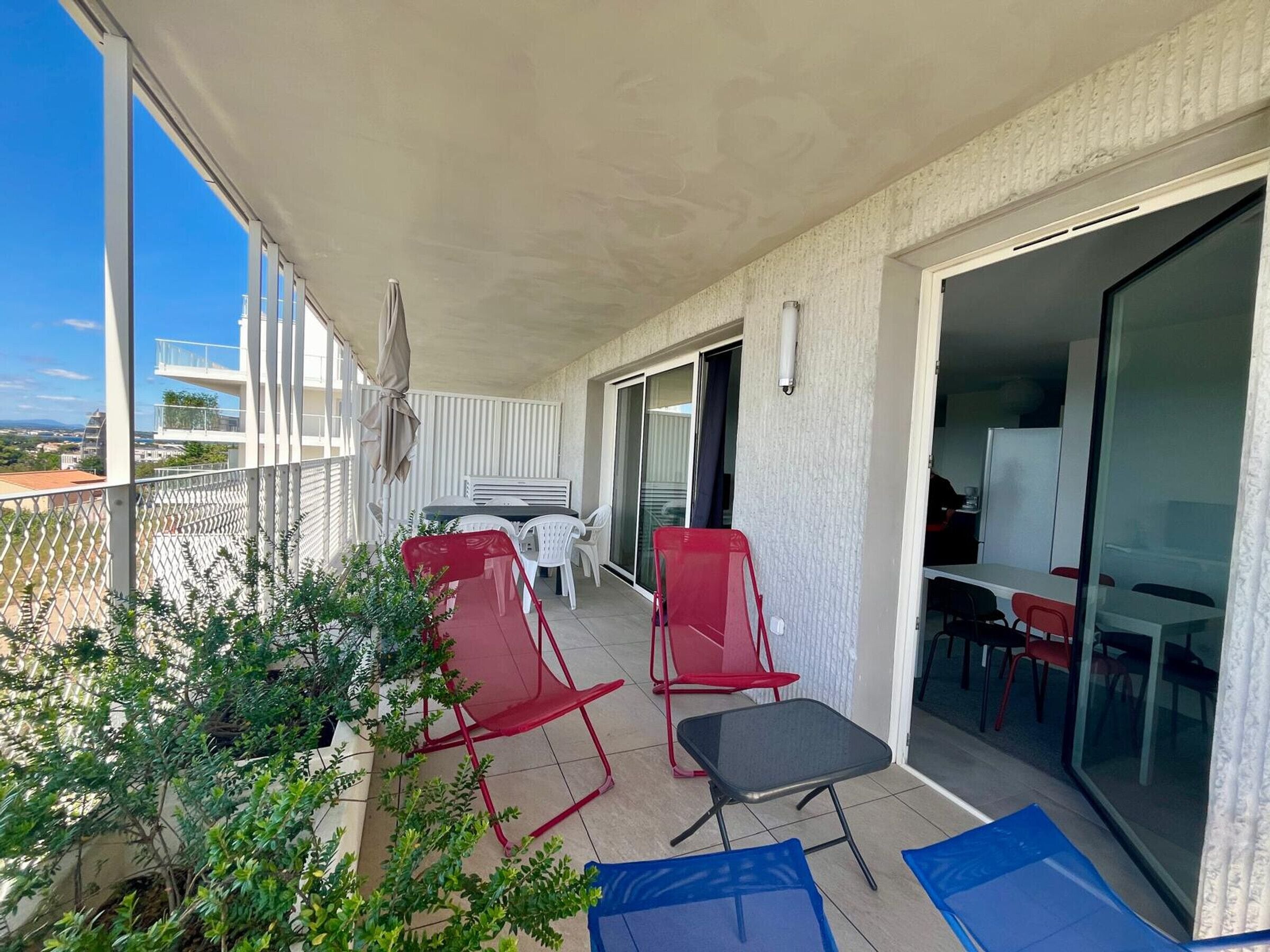 A balcony with a table and chairs, a sliding glass door leading to a room, and a view of buildings in the distance.