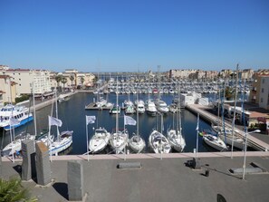 A marina with numerous boats docked, a clear sky, and buildings in the background. - Studio near the beach - 4 guests (Gruissan)