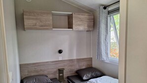 Quarto compacto com duas camas, um pequeno armário, uma tomada e uma janela com persianas.