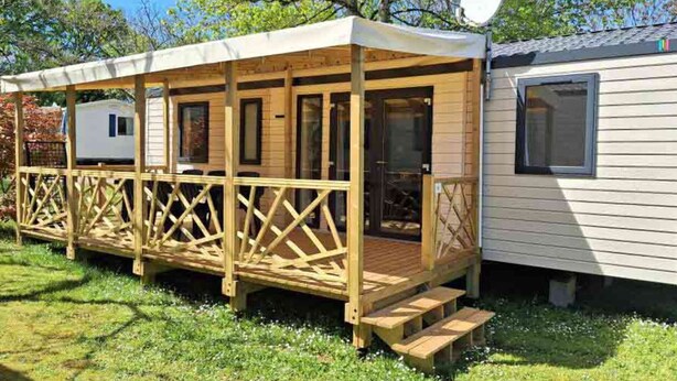 Uma casa móvel com um deck de madeira e uma antena parabólica.