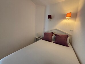 Ein Einzelbett mit weißem Kopfteil und zwei Kissen, ein Nachttisch mit Lampe sowie zwei Wandleuchten.