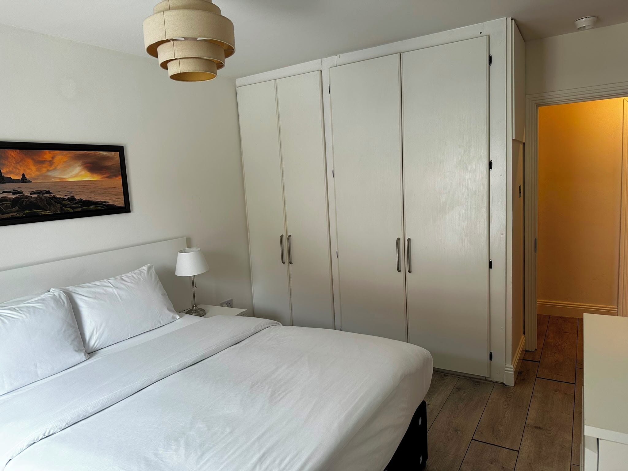 A bedroom with a bed, a nightstand, a lamp, a wardrobe, and a painting on the wall.