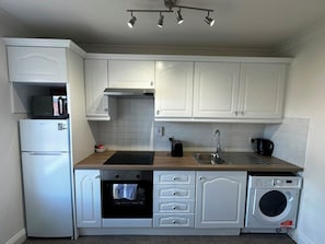 A modern kitchen with white cabinetry, a built-in oven, a microwave, a sink, and a washing machine. - Parnell District Apartments (Dublin)