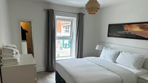 Et hotelværelse med en seng, et natbord, en lampe, et vindue med gardiner og et billede på væggen.
