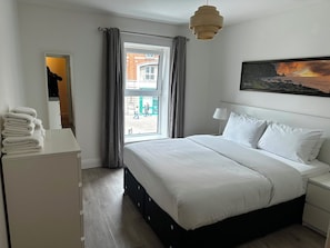 A hotel room with a bed, a bedside table, a lamp, a window with curtains, and a painting on the wall. - Parnell District Apartments (Dublin)