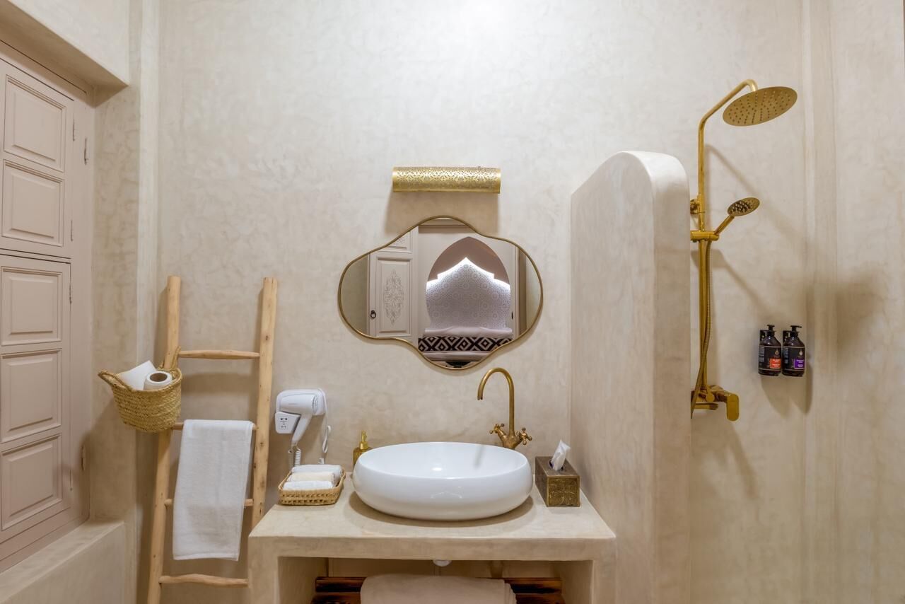 A bathroom with a round sink, a towel rack, a mirror, a showerhead, and a towel dispenser.