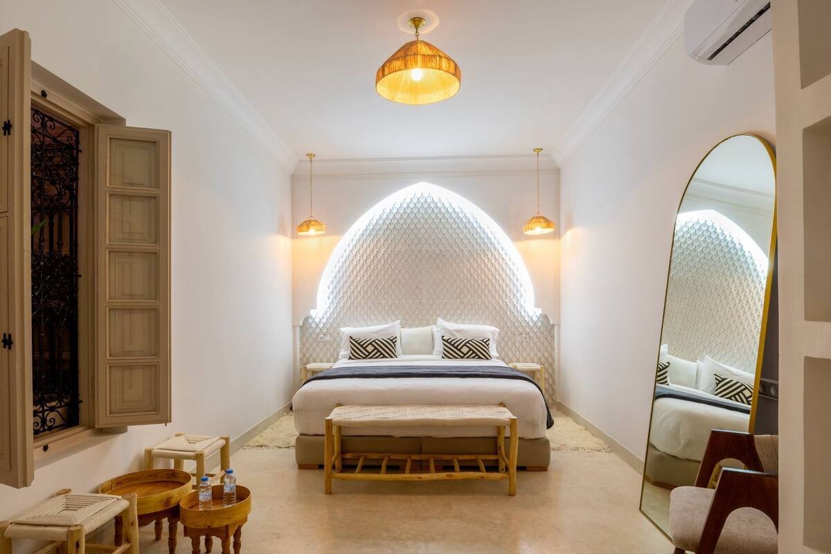 A bedroom with a bed, bedside tables, a bench, a mirror, and a decorative wall.