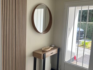 Ein Zimmer mit Holzpaneelausstattung, einem runden Spiegel, einem Holzkonsole und einer Lampe sowie einem Fenster mit Blick auf ein Auto und Grünflächen.
