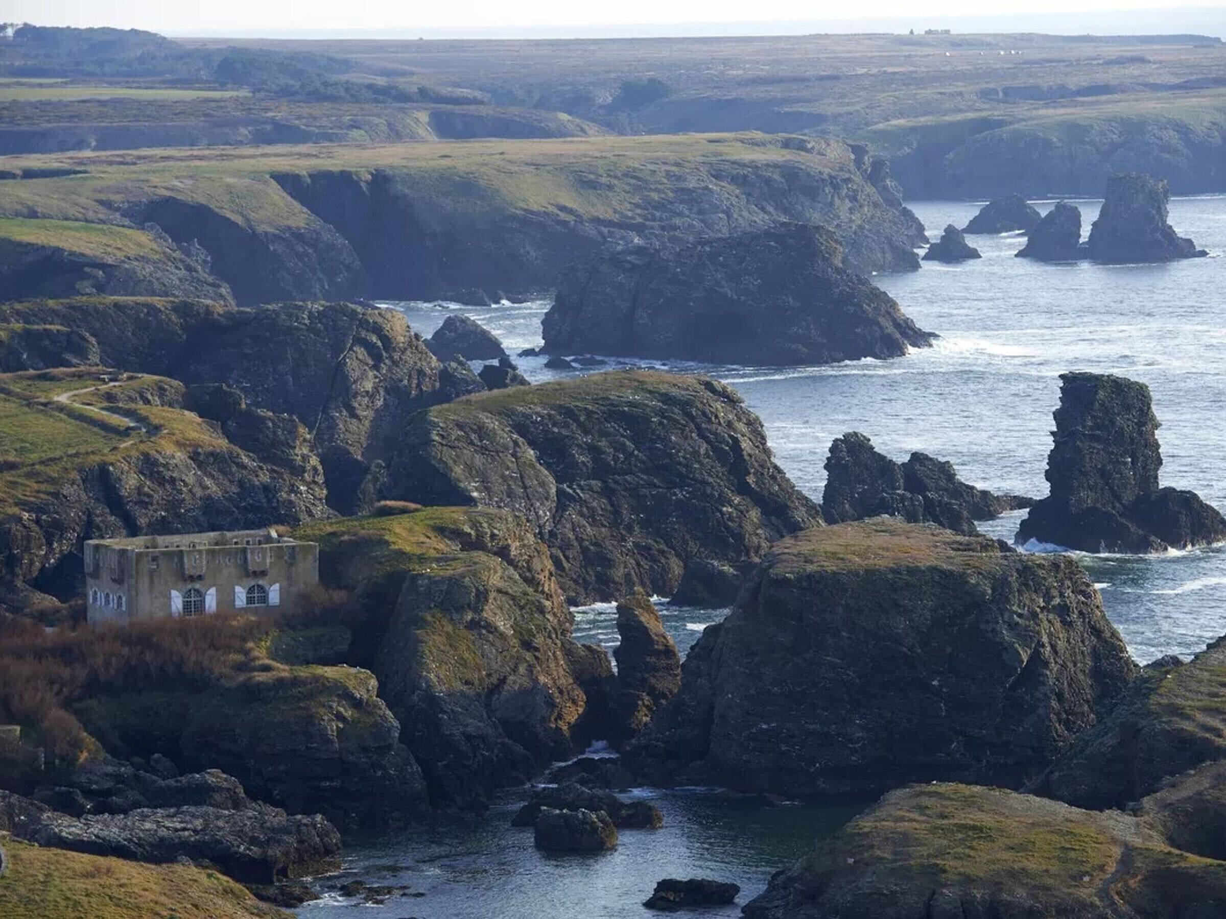 Un paysage côtier avec des falaises rocheuses et un bâtiment doté d’une fenêtre visible.