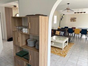 Ein modernes Wohnzimmer mit einer Holzbücherwand, einem Glastisch und einem Essbereich mit Stühlen und einer Couch.
