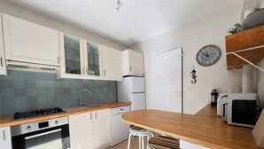Cocina moderna con armarios blancos, encimera de madera, horno empotrado, lavavajillas y una zona de bar con taburetes.