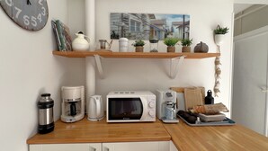 Una cocina con microondas, cafetera, hervidor y estantes con plantas y utensilios de cocina.