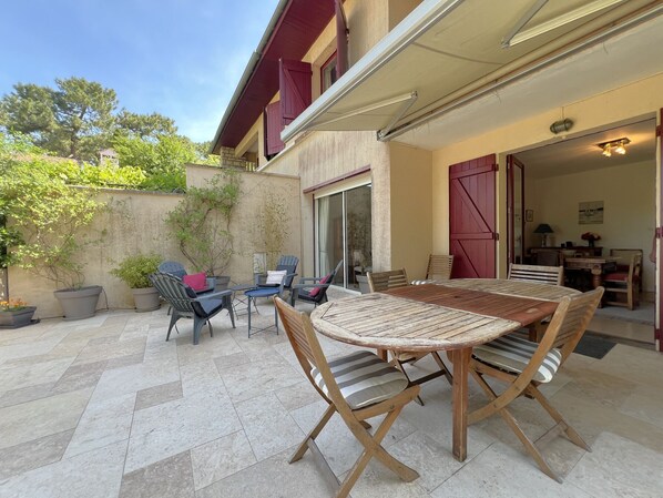 Eine Terrasse im Freien mit Holztisch und -stühlen, einer Schiebetür und Blumentöpfen.