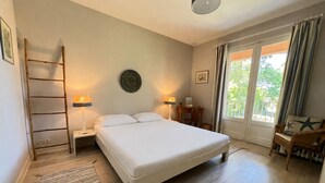Un dormitorio con cama, mesitas de noche, escritorio, silla, escalera y vista por la ventana.