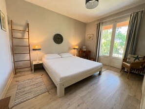 Ein Schlafzimmer mit Bett, Nachttischen, Schreibtisch, Stuhl, einer Leiter und Blick durch ein Fenster.