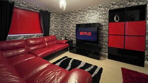 A living room with a red sofa, a TV displaying 'NETFLIX,' and a wall with a money-themed wallpaper. - The Coach-House, Lincoln Central + Parking, walking distance to all attractions (Lincoln)