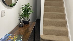 A staircase with beige carpeted steps, a wooden table with a magazine, a potted plant, and a round mirror on the wall. - The Coach-House, Lincoln Central + Parking, walking distance to all attractions (Lincoln)