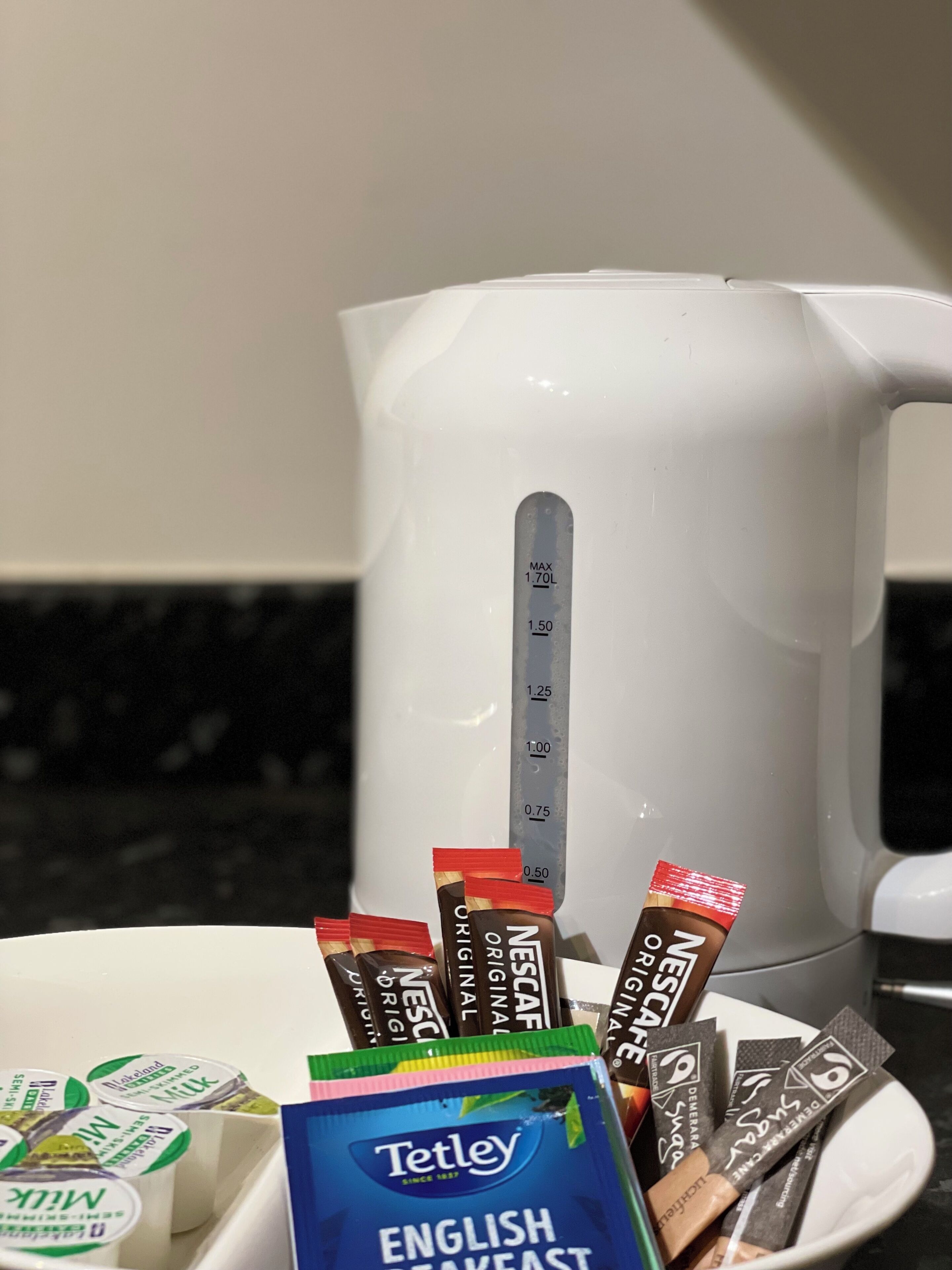 Une machine à café blanche avec des repères de mesure, une assiette contenant différentes capsules de café et une boîte de thé Tetley English Breakfast.
