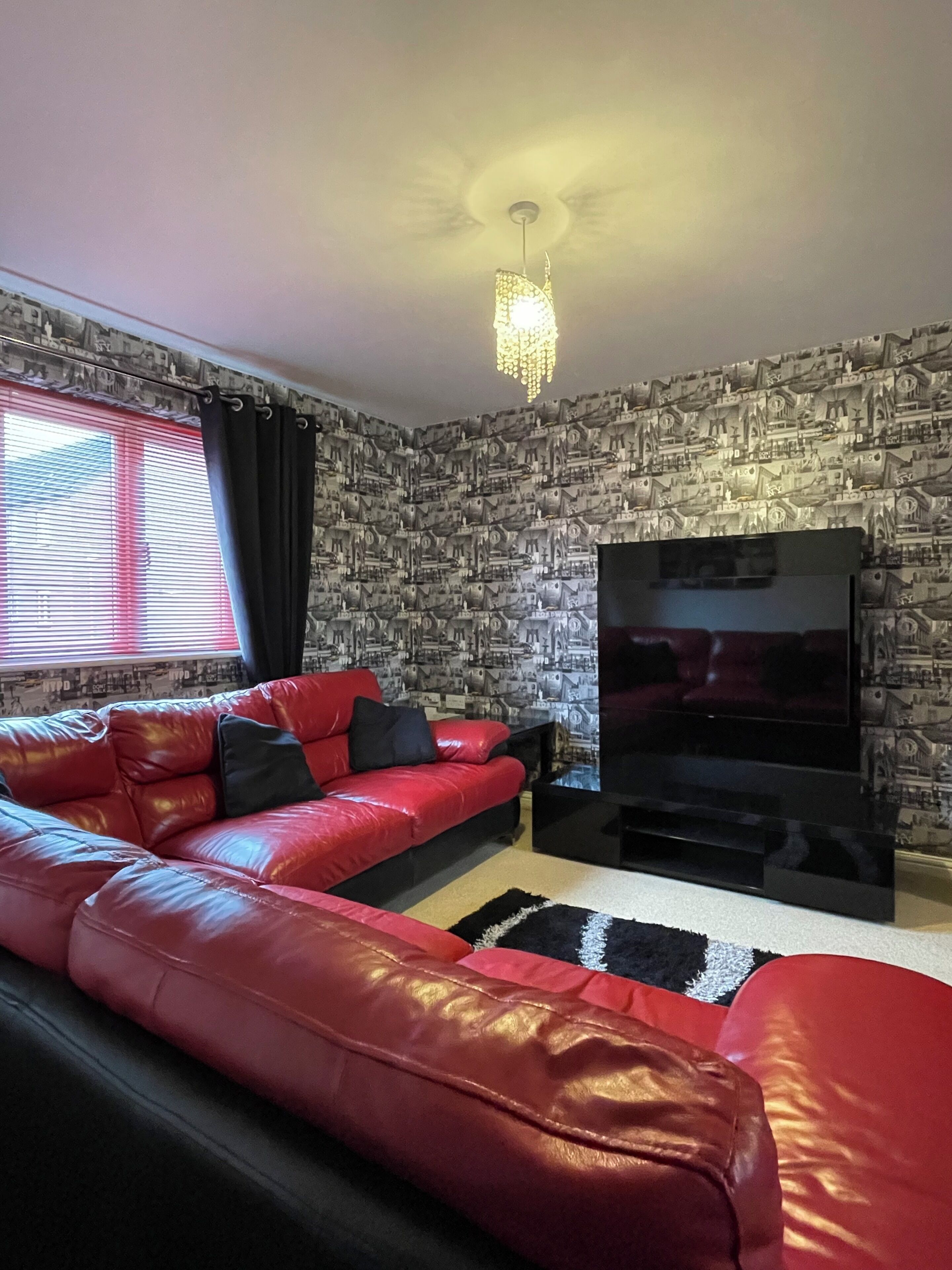 A living room with a red leather sofa, a flat-screen TV, and a patterned wallpaper.