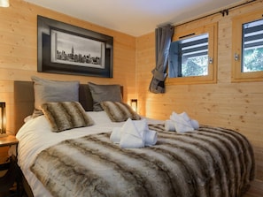 Ein Holzhütten-Zimmer mit einem Bett, einem gerahmten Stadtbild und einem Fenster mit Vorhängen.