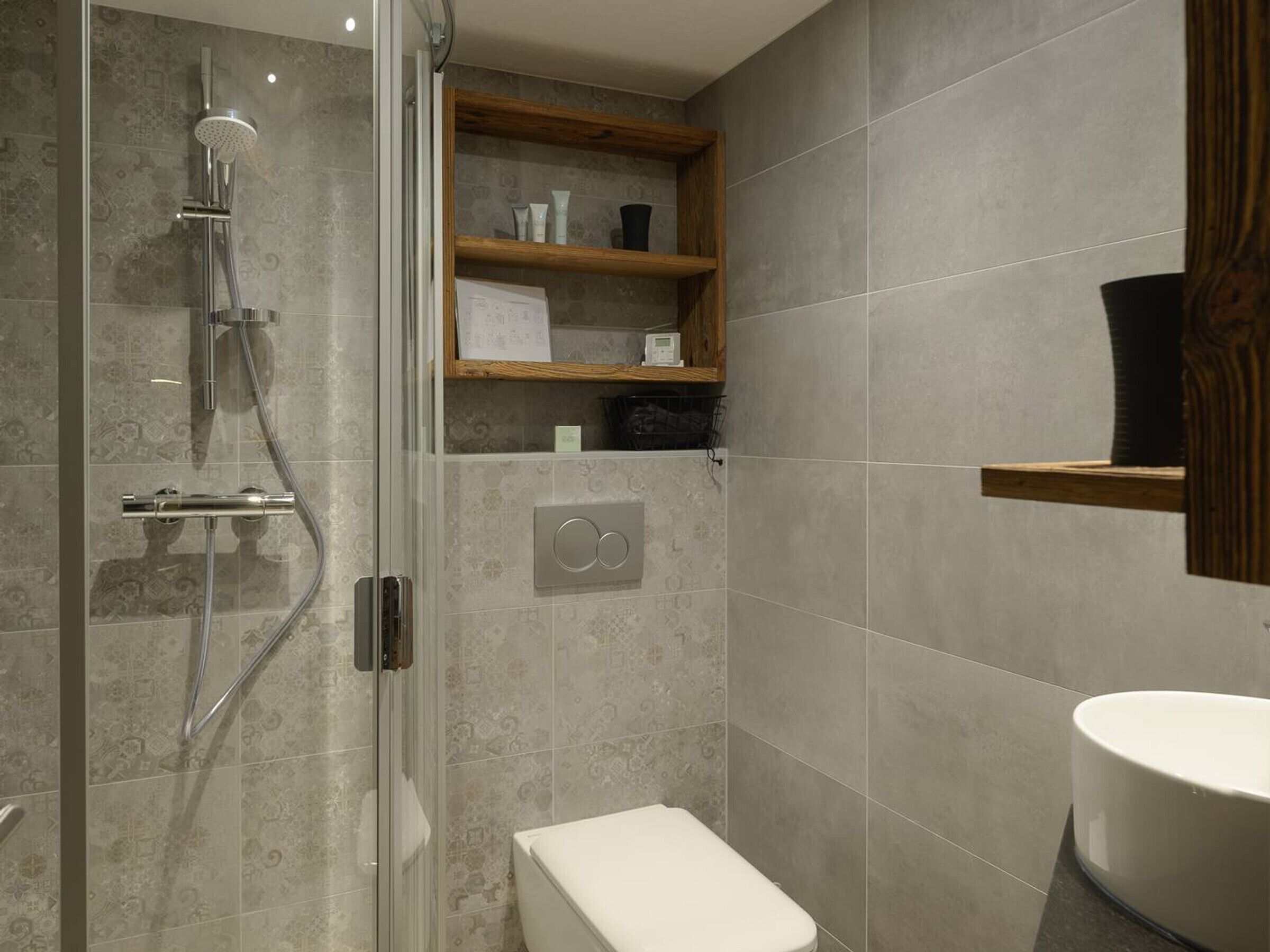 A modern bathroom with a glass-enclosed shower, a toilet, and a wooden shelf with toiletries.