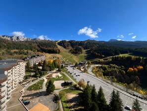 A residential area with apartment buildings, a parking lot, and a road leading to a mountainous landscape. - Authentic Vercors Getaway – Ski, Hiking, Cycling – Slopeside Apartment for 6 (Villard-de-Lans)