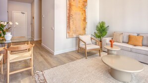 Un salon moderne avec une table à manger en verre, des chaises en bois, un canapé gris et un grand tableau abstrait accroché au mur.