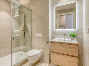 A modern bathroom with a glass-enclosed shower, a white toilet, a wooden vanity with a sink, and a mirror above the vanity. - Spacious studio near the port - Estepona (Estepona)