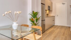 Une cuisine moderne avec des meubles blancs, une table à manger en verre et une plante.